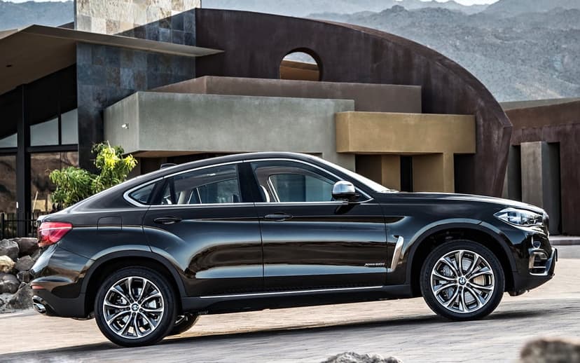 Profile view of a dark luxury SUV parked before a modern multi-textured house with mountains in the background.