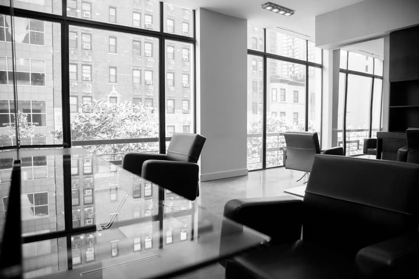 Contemporary armchairs and sofa arranged in a monochrome office lounge facing tall windows with a city view.