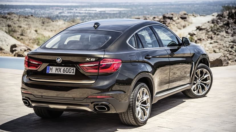 Dark metallic BMW X6 luxury SUV parked on stone pavers with a scenic rocky desert valley background.