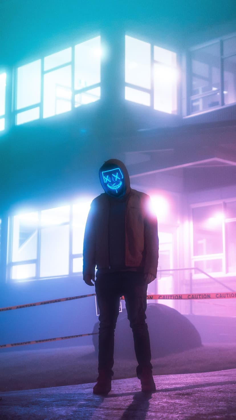Masked character with glowing blue X-eyes stands behind yellow caution tape amidst neon urban lighting.