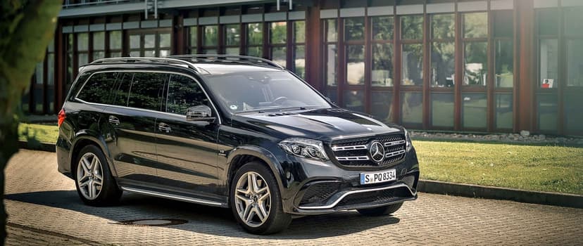 Black Mercedes-Benz GLS 63 AMG SUV parked on cobblestone with a glass building and soft sunlight background.