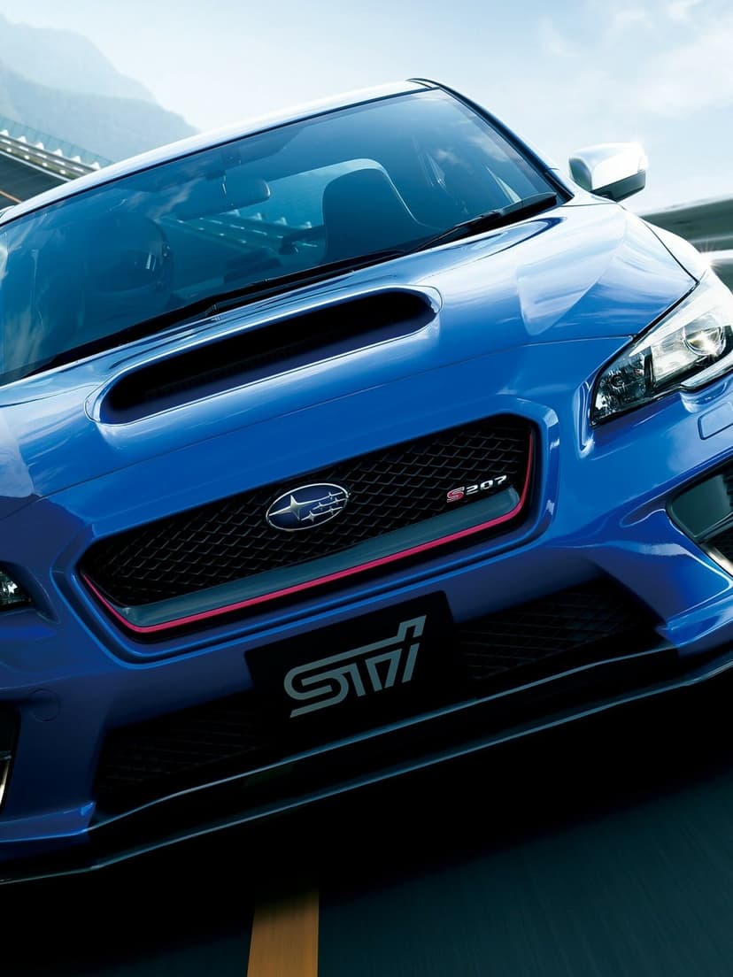 Front view of a blue Subaru WRX STI S207 with red grille accents and a large hood scoop on a road.