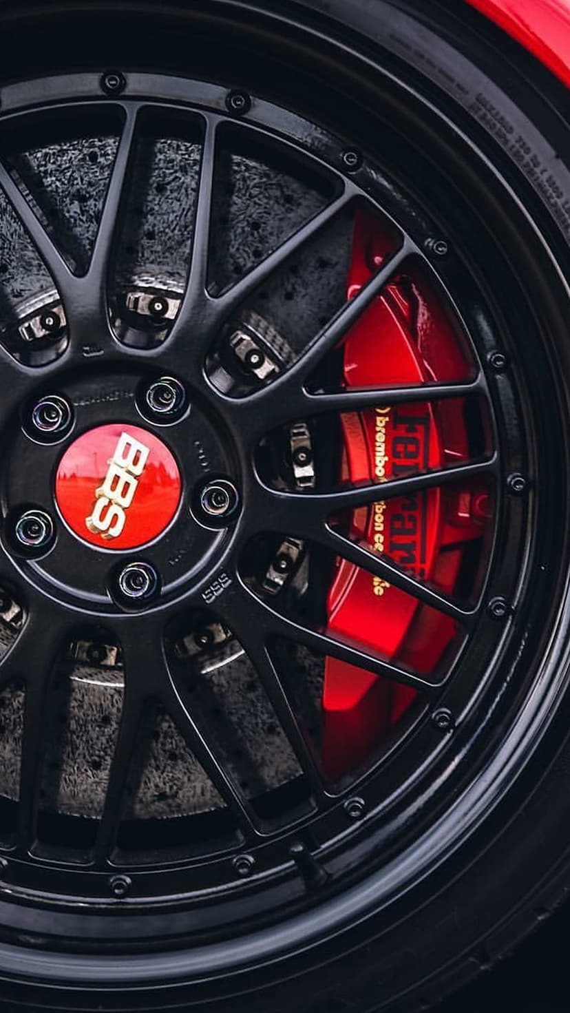 Ferrari red Brembo brake calipers and black multi-spoke BBS alloy wheel shown in a detailed vertical close-up.