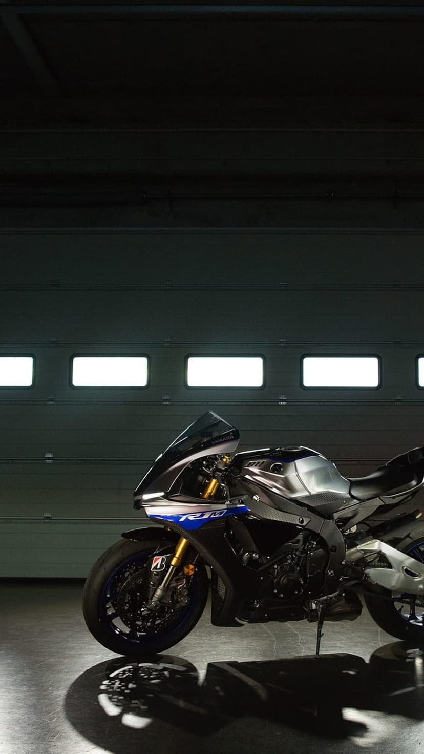 Yamaha R1 sportbike with silver fairings and blue wheels parked inside a dimly lit garage with glowing panels.