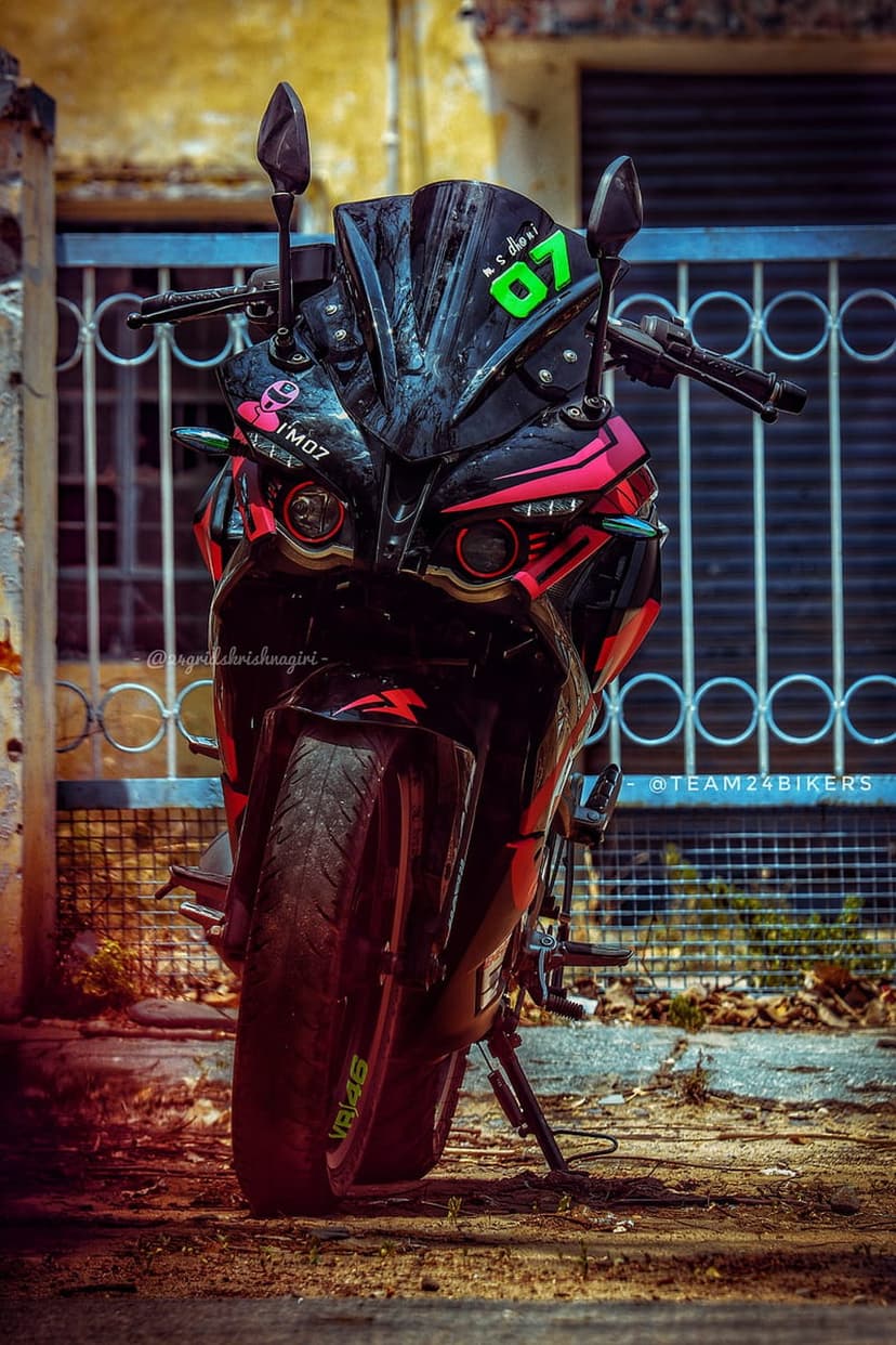Black and pink sport motorcycle with racing number 07 parked in front of a blurred metal gate at a low angle.