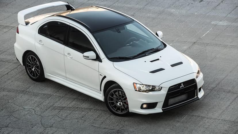 White Mitsubishi Lancer Evolution X with a black roof and large spoiler parked on a gray concrete surface.