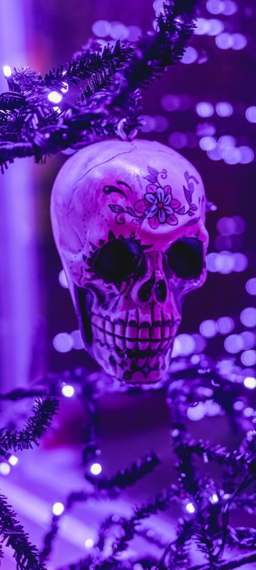 Purple sugar skull ornament with intricate patterns hanging from a branch illuminated by violet fairy lights.