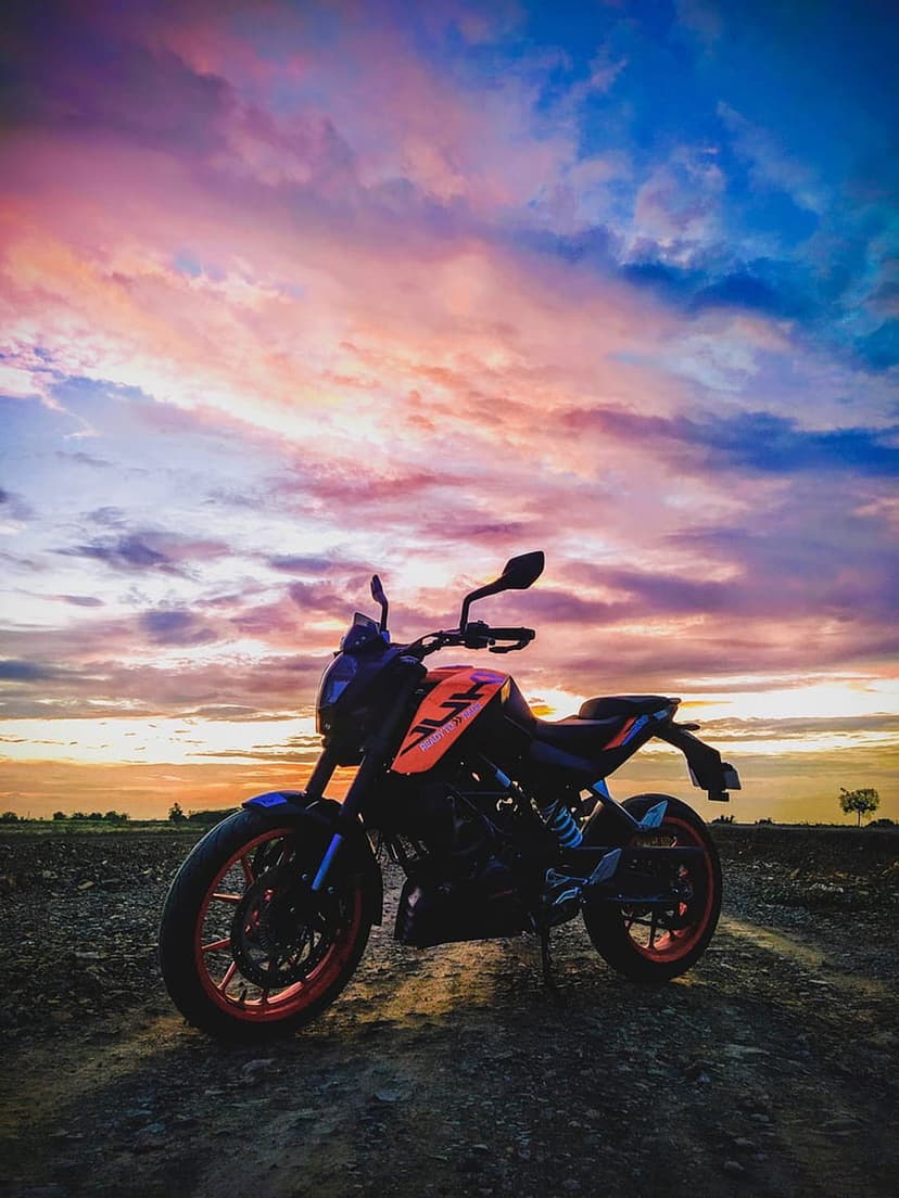 Motorcycle silhouette on a gravel road under a vibrant pink and orange sunset sky with wispy clouds.