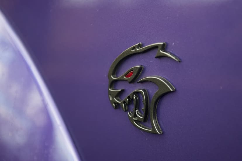 Black Dodge Hellcat emblem with a red eye on a metallic purple car fender with soft natural lighting and depth.