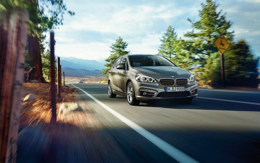 Silver BMW car driving fast on a winding mountain road with motion blur and distant peaks under a blue sky.
