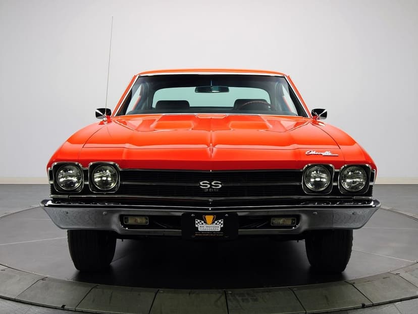 Front view of a bright orange 1969 Chevrolet Chevelle SS 396 with chrome trim and black grille in a studio.