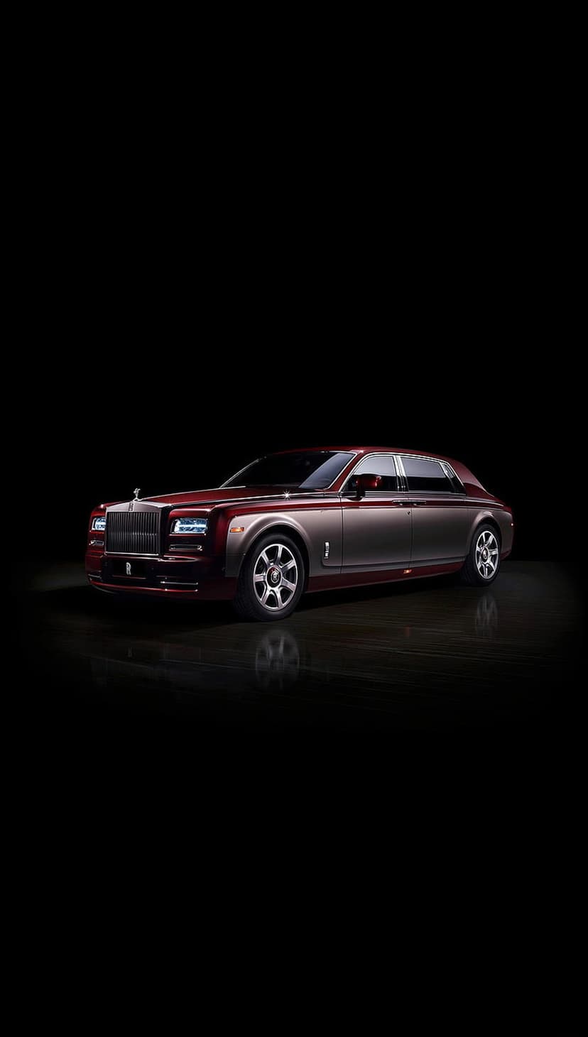 Rolls-Royce Phantom luxury sedan with crimson and silver two-tone exterior and glowing headlights in a dark studio.