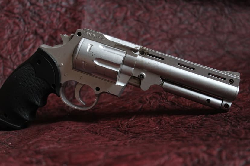 Silver revolver with a black grip lies on a textured red background, showcasing the metallic cylinder and barrel.