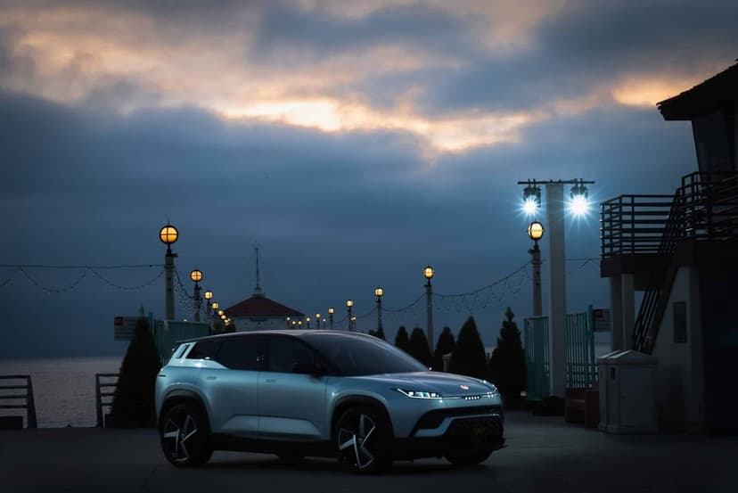 Sleek silver electric SUV on a coastal pier at dusk with glowing globe lamps and a dramatic sunset sky.