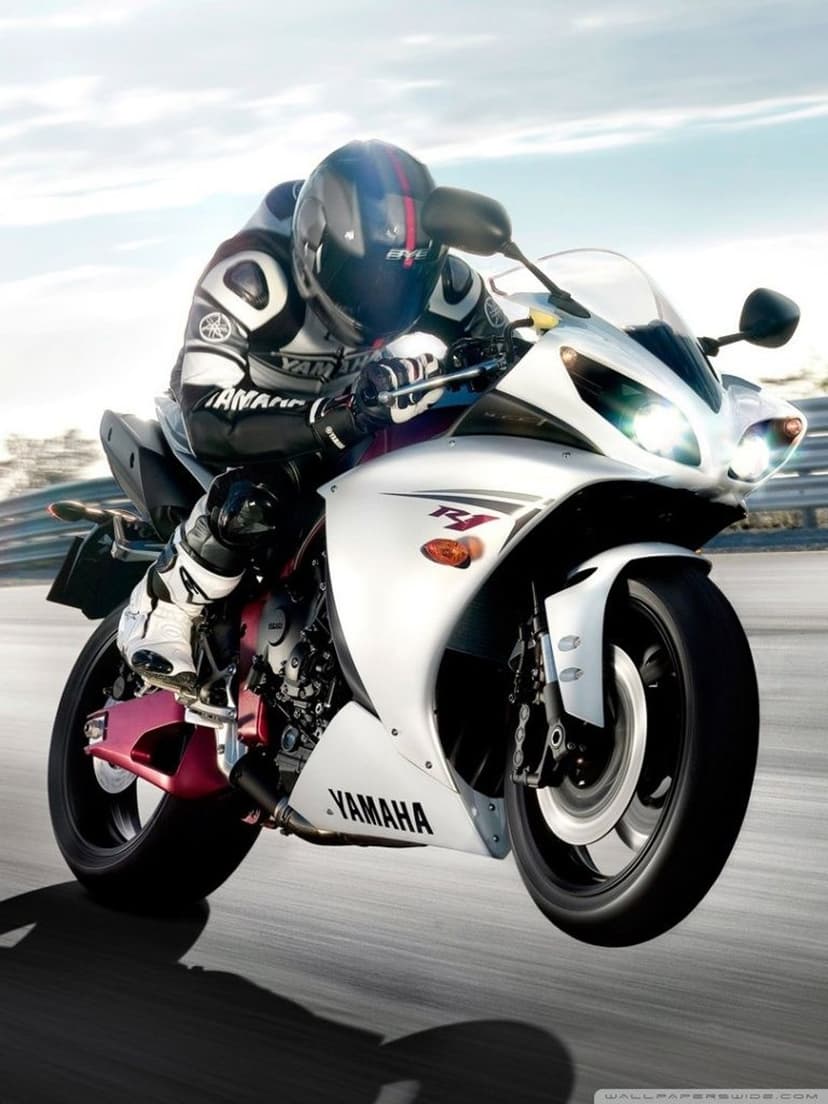 Professional racer on a white Yamaha R1 sportbike leans deeply into a paved track corner under a bright sky.