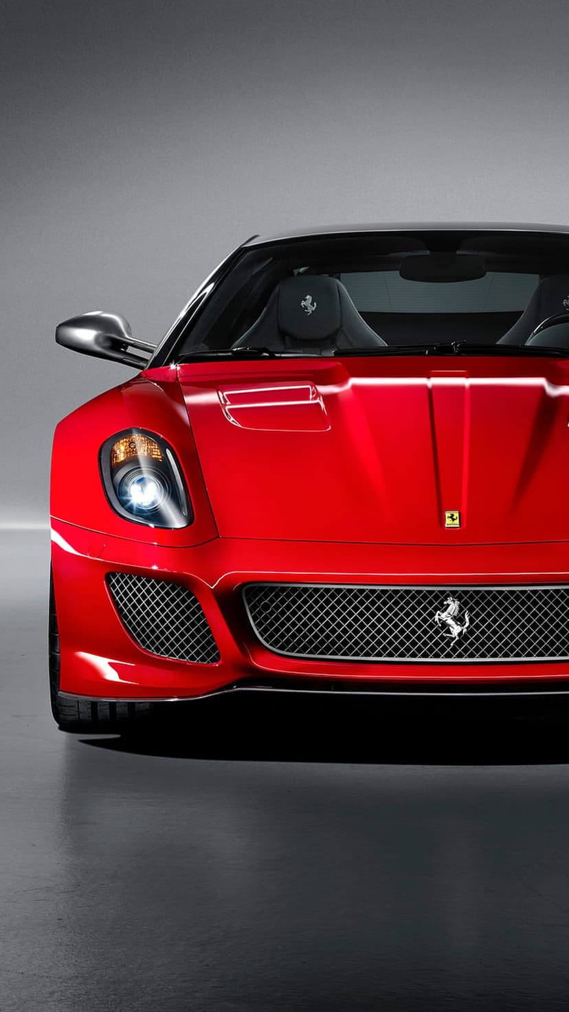 Red Ferrari 599 GTO front grille and headlights reflecting on a dark floor in a vertical automotive portrait.