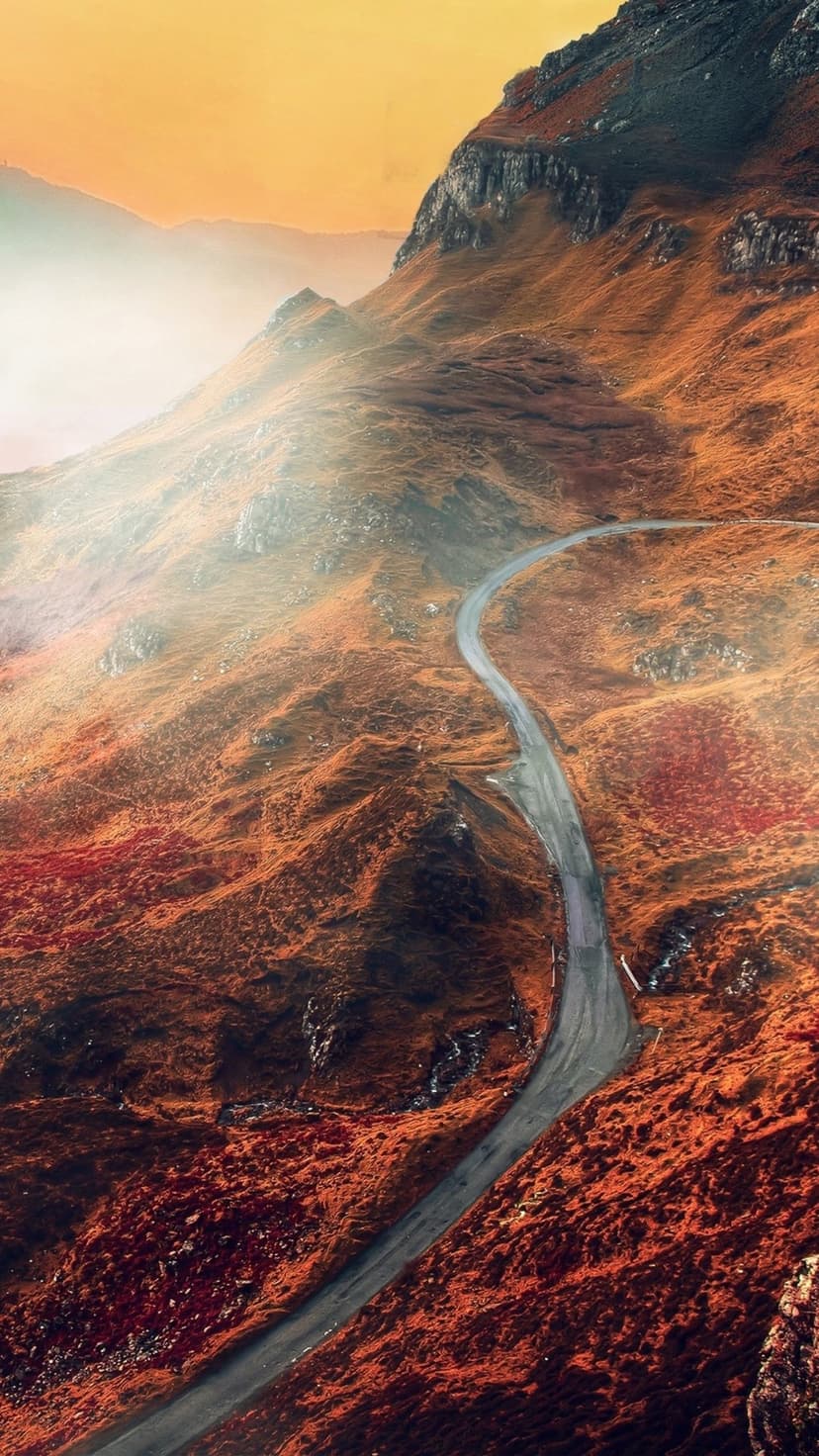 Winding mountain road curving through jagged russet peaks under soft light in a vertical landscape view.