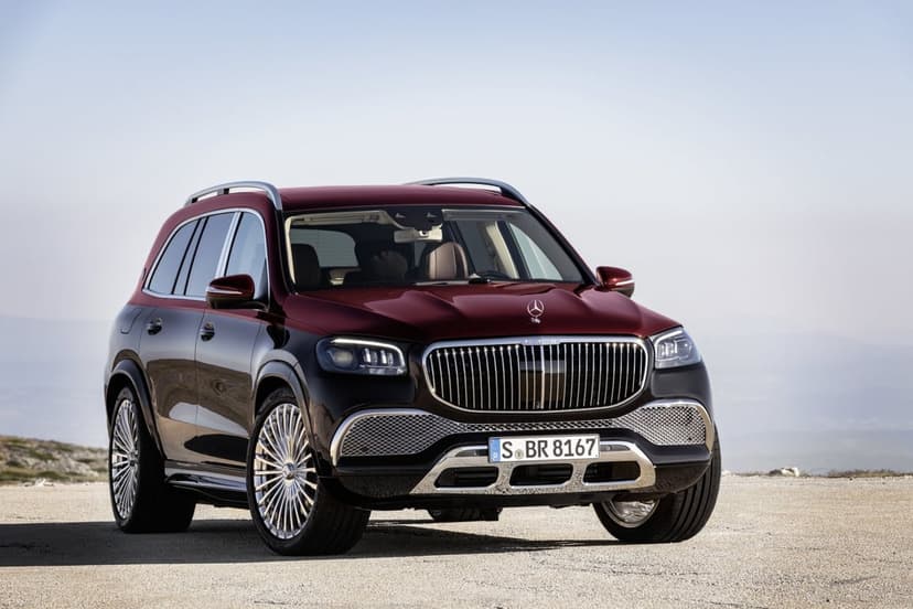 Two-tone burgundy and black Mercedes-Maybach GLS 600 SUV parked on a light gravel road under a clear sky.