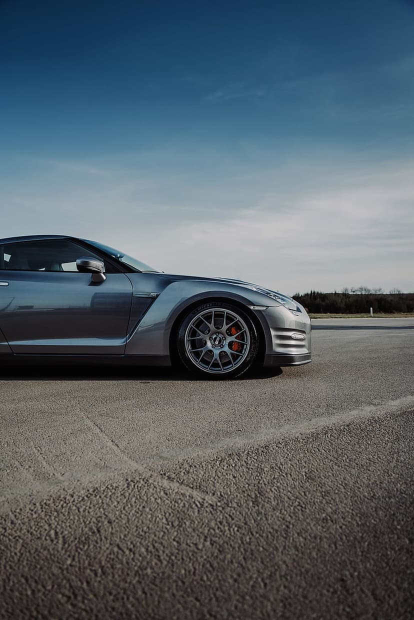 Silver Nissan GT-R sports car on asphalt with red brake calipers and alloy wheels under a clear blue sky.