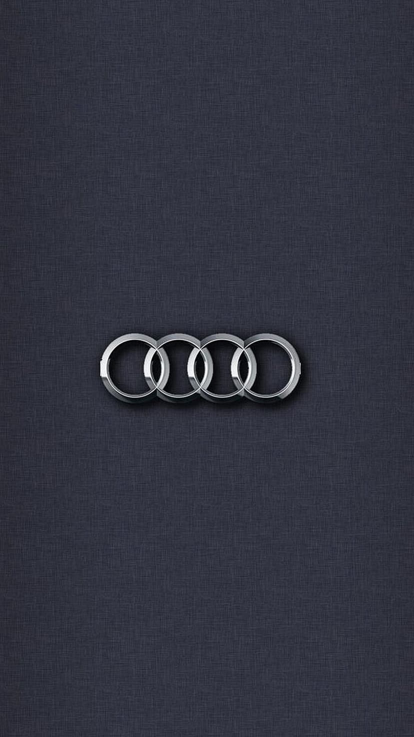 Interlocking silver rings of the Audi logo centered on a dark, grainy textured surface with soft lighting.