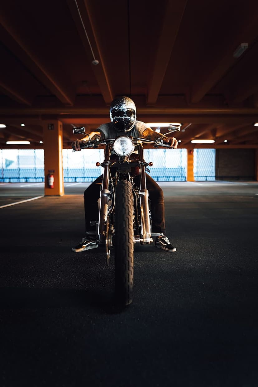 Biker on a vintage motorcycle with a glowing headlight inside a dark concrete parking garage with industrial pillars.