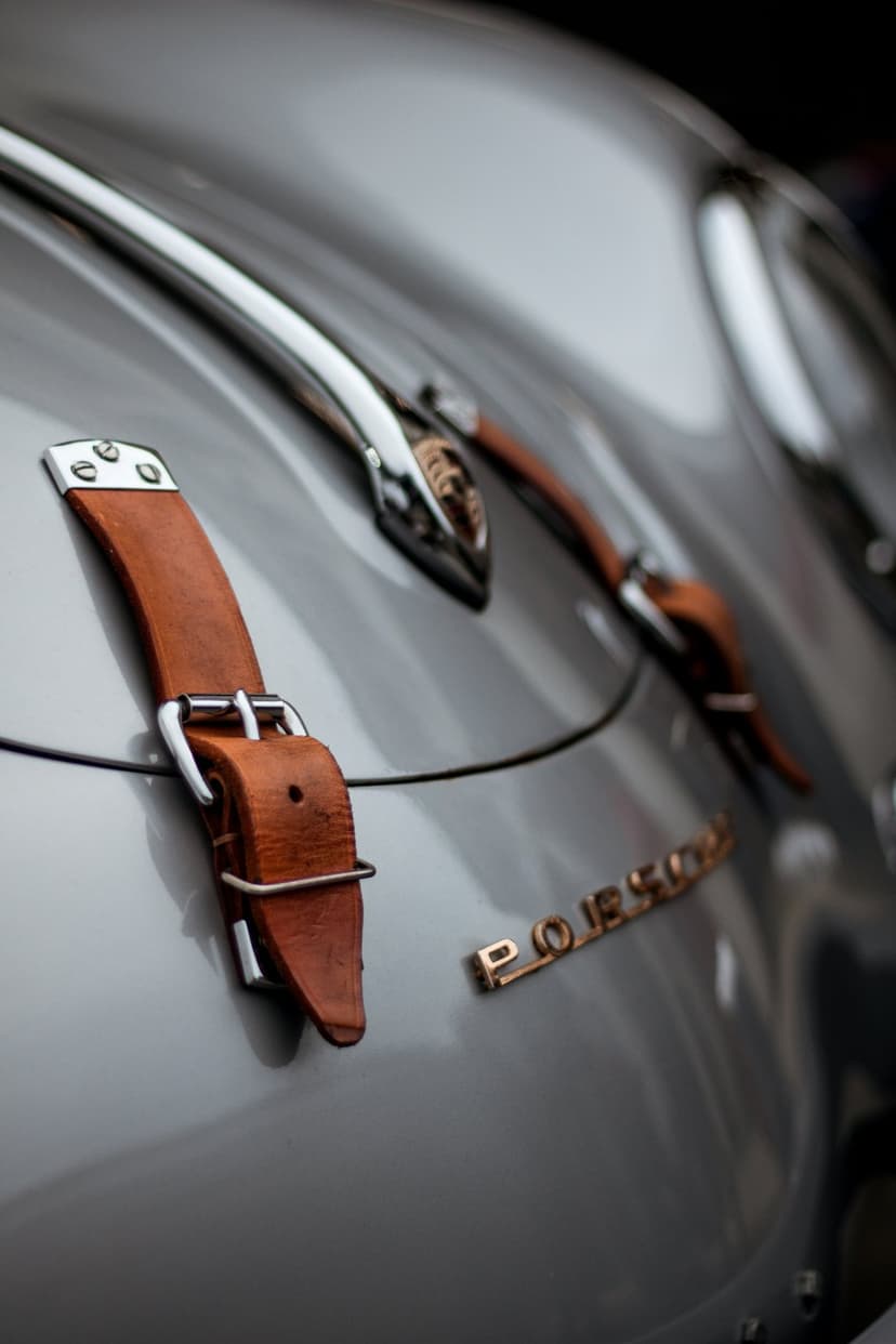 Silver Porsche rear trunk detail featuring brown leather straps and a gold crest emblem with chrome trim accents.