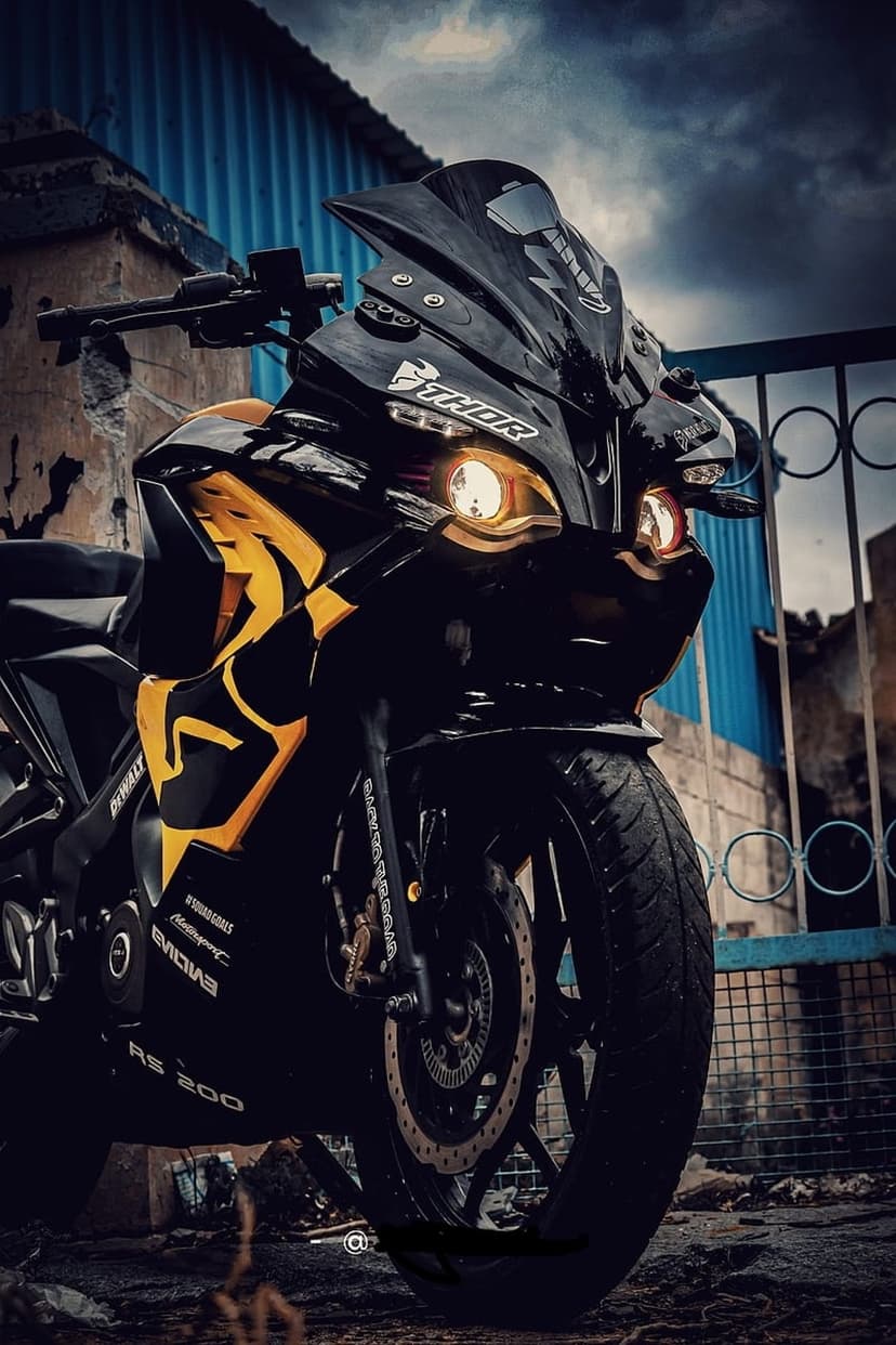 Yellow sports motorcycle with illuminated headlights and a black chassis parked in a dark, moody environment.