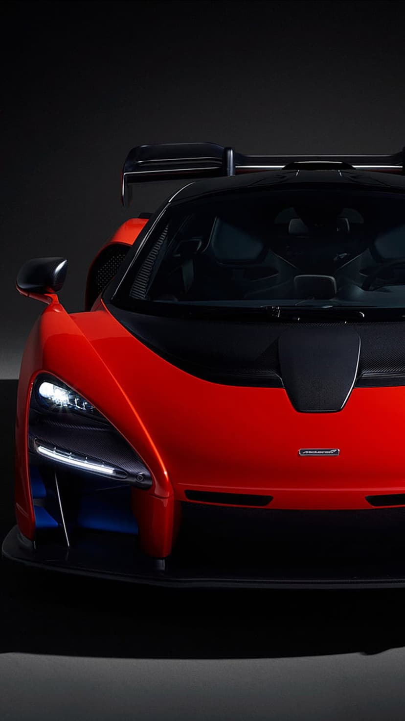 McLaren Senna hypercar in scarlet red shows aggressive aerodynamic lines and LED headlights on a dark background.