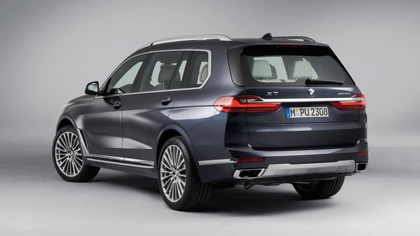 Dark blue BMW X7 luxury SUV parked in a grey studio showing its rear profile and silver alloy wheels.