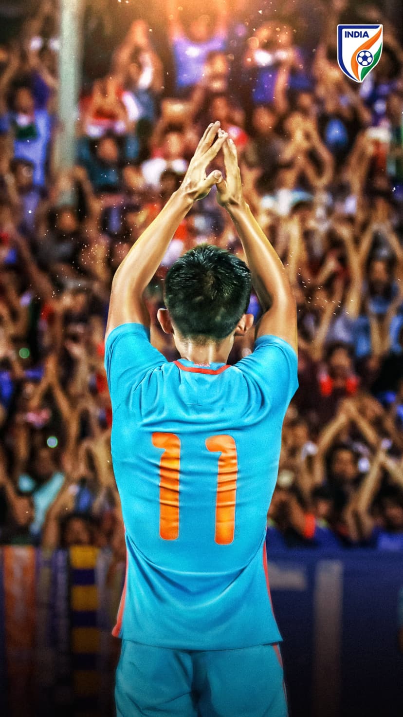 Footballer in a blue number eleven jersey raises his hands toward a cheering stadium crowd at night.