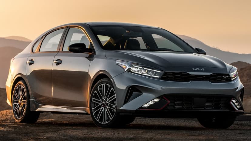 Grey Kia Forte GT sedan parked on a dirt path with sunset lighting and mountain silhouettes in the background.