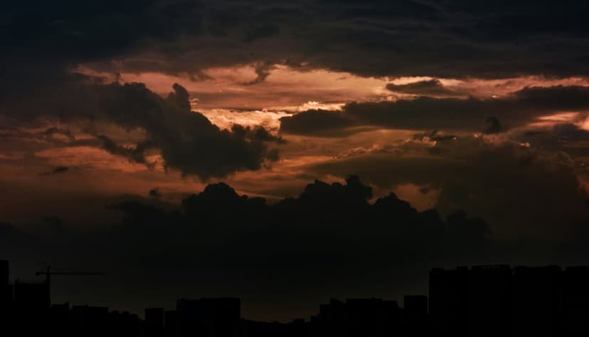 Radiant orange clouds contrast with dark storm fronts over a silhouetted metropolitan skyline at twilight.
