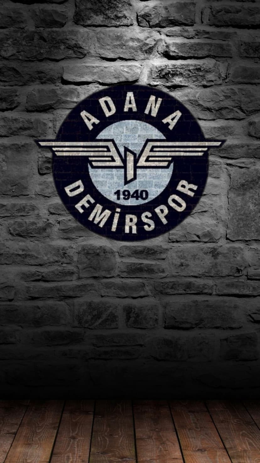 Adana Demirspor 1940 logo with wings on a dark gray brick wall above a rustic wooden floor with moody shadows.