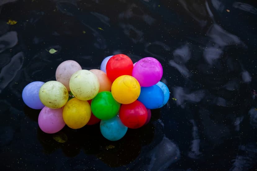 Multi-colored balloons floating on a dark reflective water surface with subtle ripples and deep shadows.