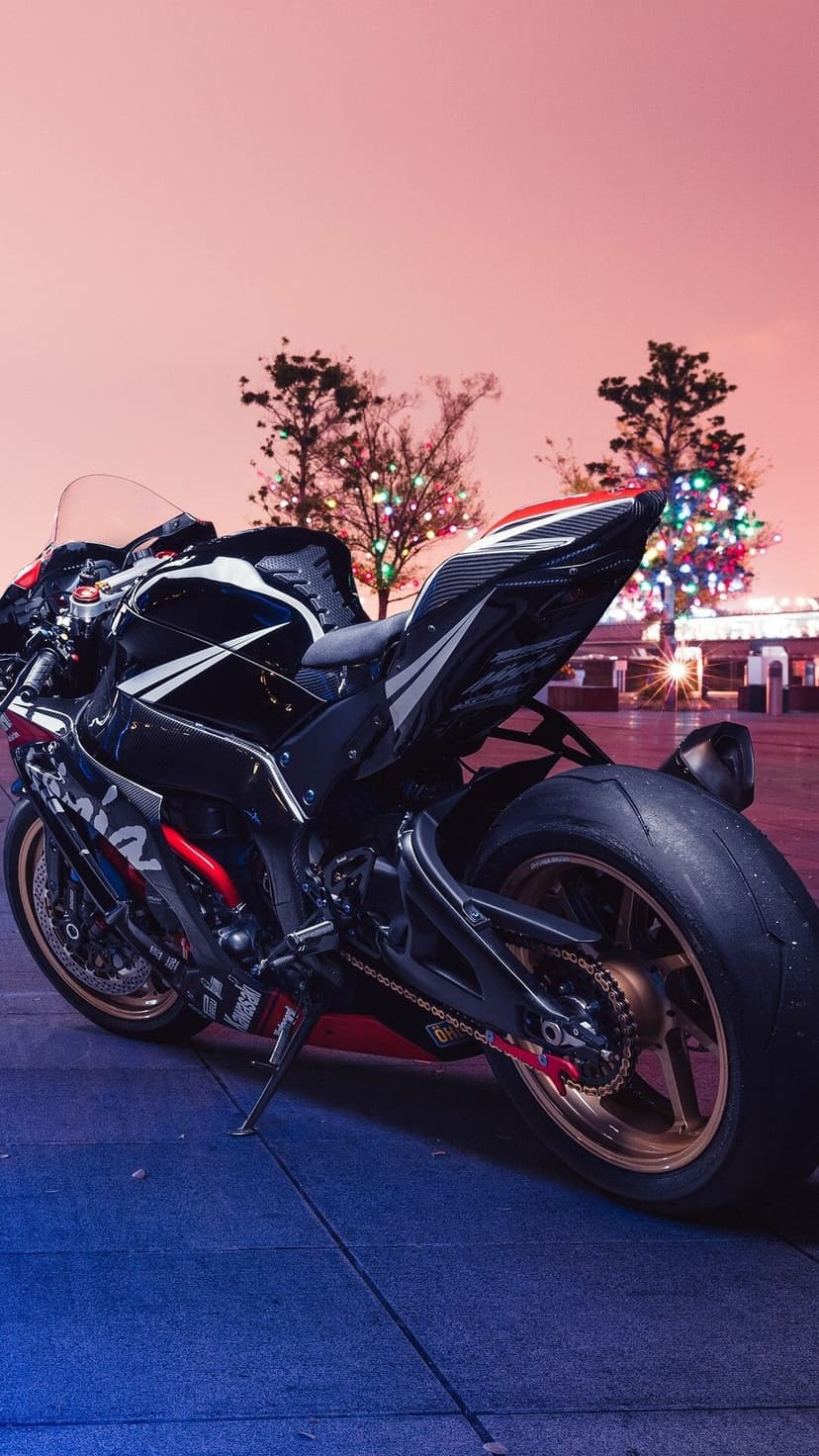 Black and red Kawasaki Ninja sportbike with racing tires parked at night under a pink sky with bokeh lights.