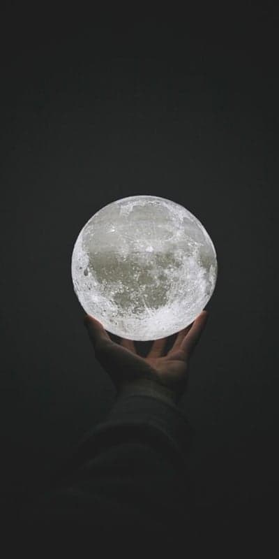Hand holding glowing moon light against dark background