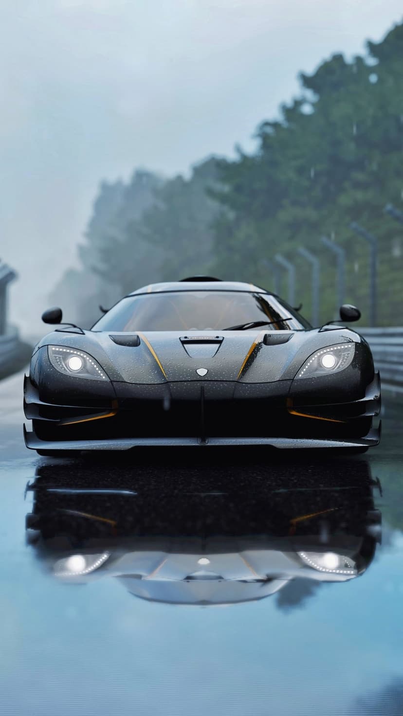 Black Koenigsegg supercar with gold accents reflects on a wet race track under a stormy gray sky during rainfall.