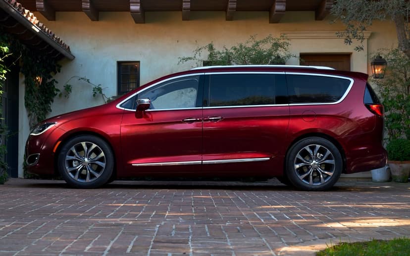 Red Chrysler Pacifica minivan parked on a brick driveway in front of a Mediterranean-style house at sunset.