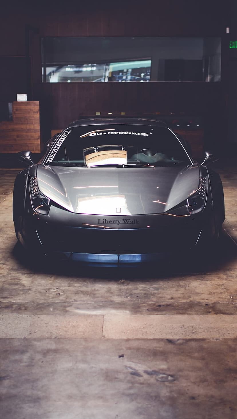 Grey Ferrari 458 Italia with a widebody kit sits in a dimly lit garage with subtle reflections on the floor.
