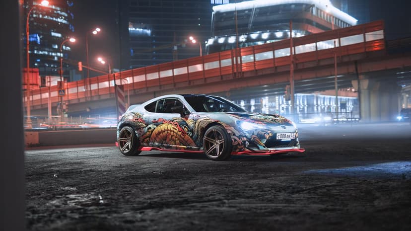 Modified sports car with dragon wrap and bronze wheels on a misty night city street under red neon lights.