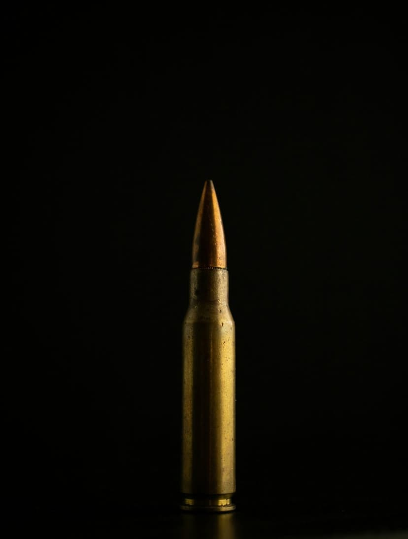 Golden brass bullet stands vertically against a solid black background with dramatic side lighting on its casing.