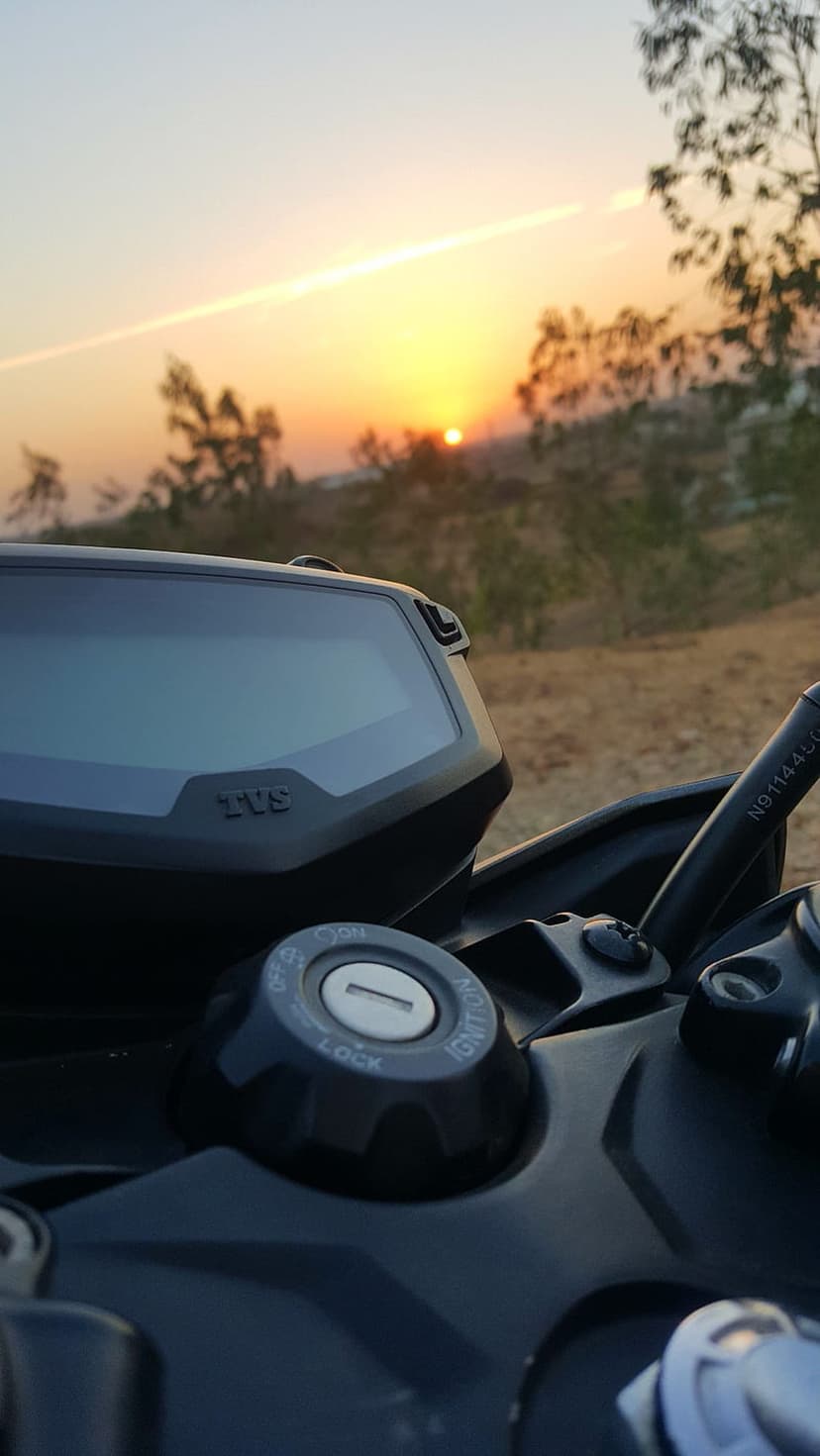 Motorcycle digital dashboard and ignition key glowing under a warm orange sunset over a dusty desert landscape.