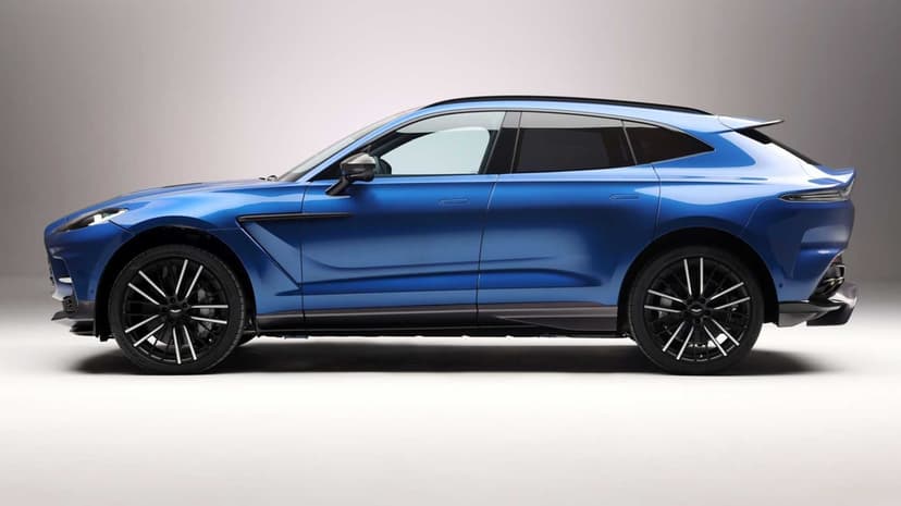 Side profile of a metallic blue Aston Martin DBX707 luxury SUV on a white studio background with black wheels.