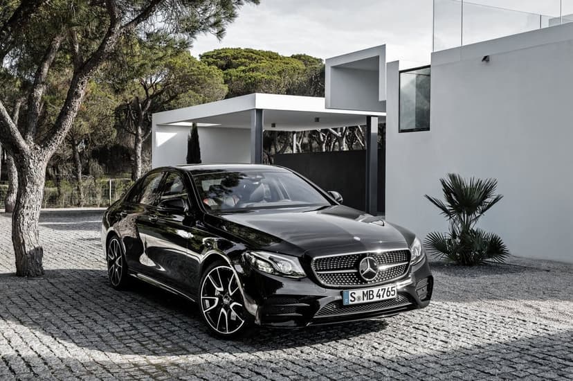 Black Mercedes-Benz E-Class sedan parked on cobblestones in front of a modern white minimalist building.