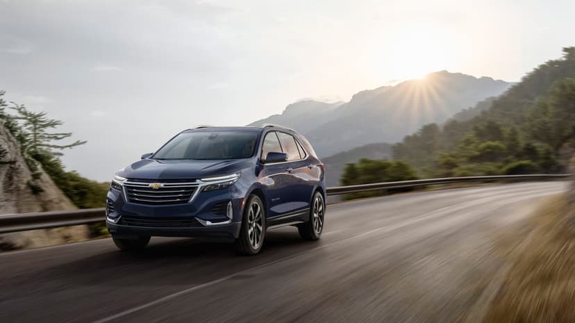 Blue SUV driving on a winding mountain road with sunrays shining over green hills at golden hour.