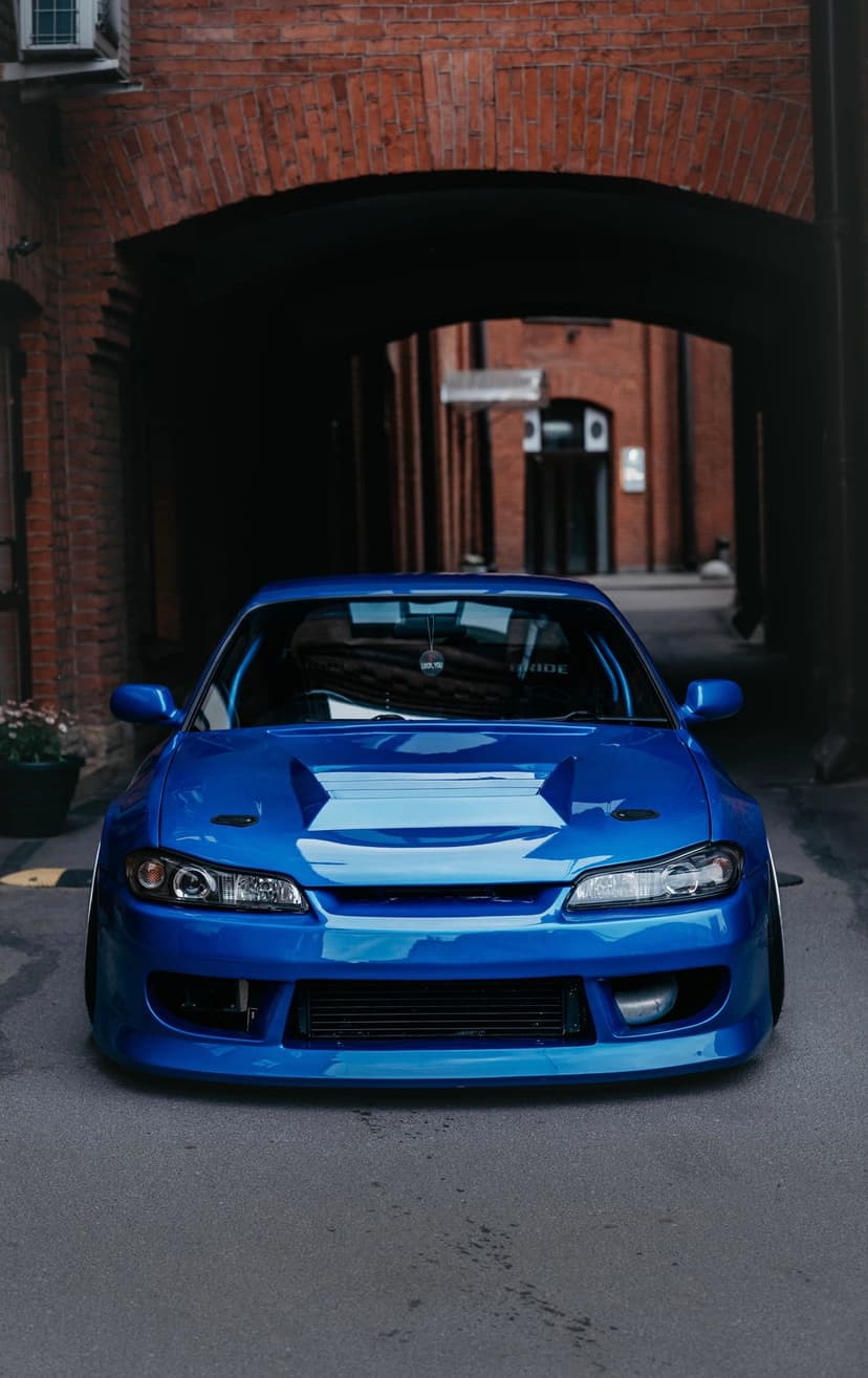 Blue Nissan S15 Silvia sports car with a widebody kit parked under a dark arched brick tunnel in an urban alley.