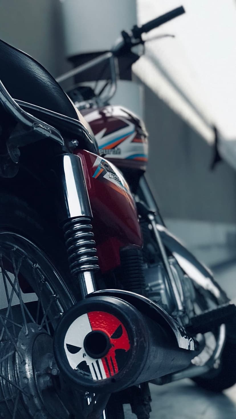 Punisher skull emblem on a red motorcycle exhaust pipe with chrome suspension and wire spokes in outdoor light.