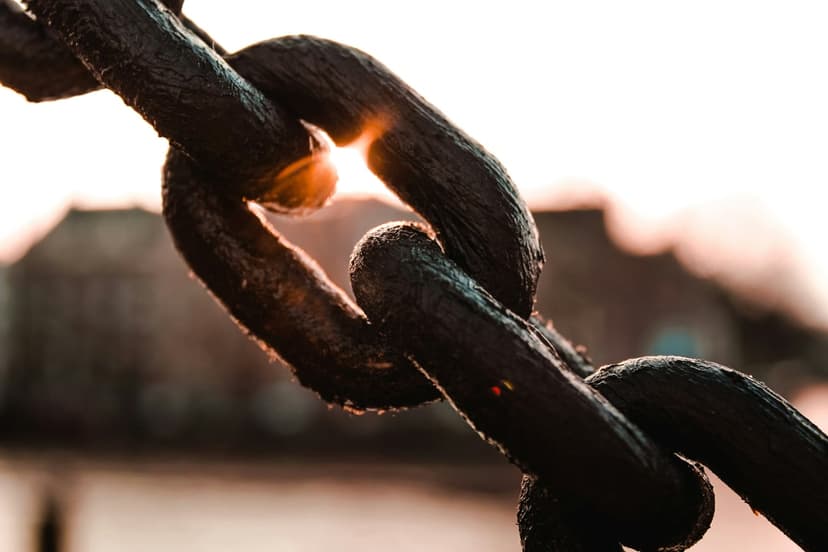 Rusty iron chain links glow as golden sunlight filters through the gaps against a soft bokeh background.