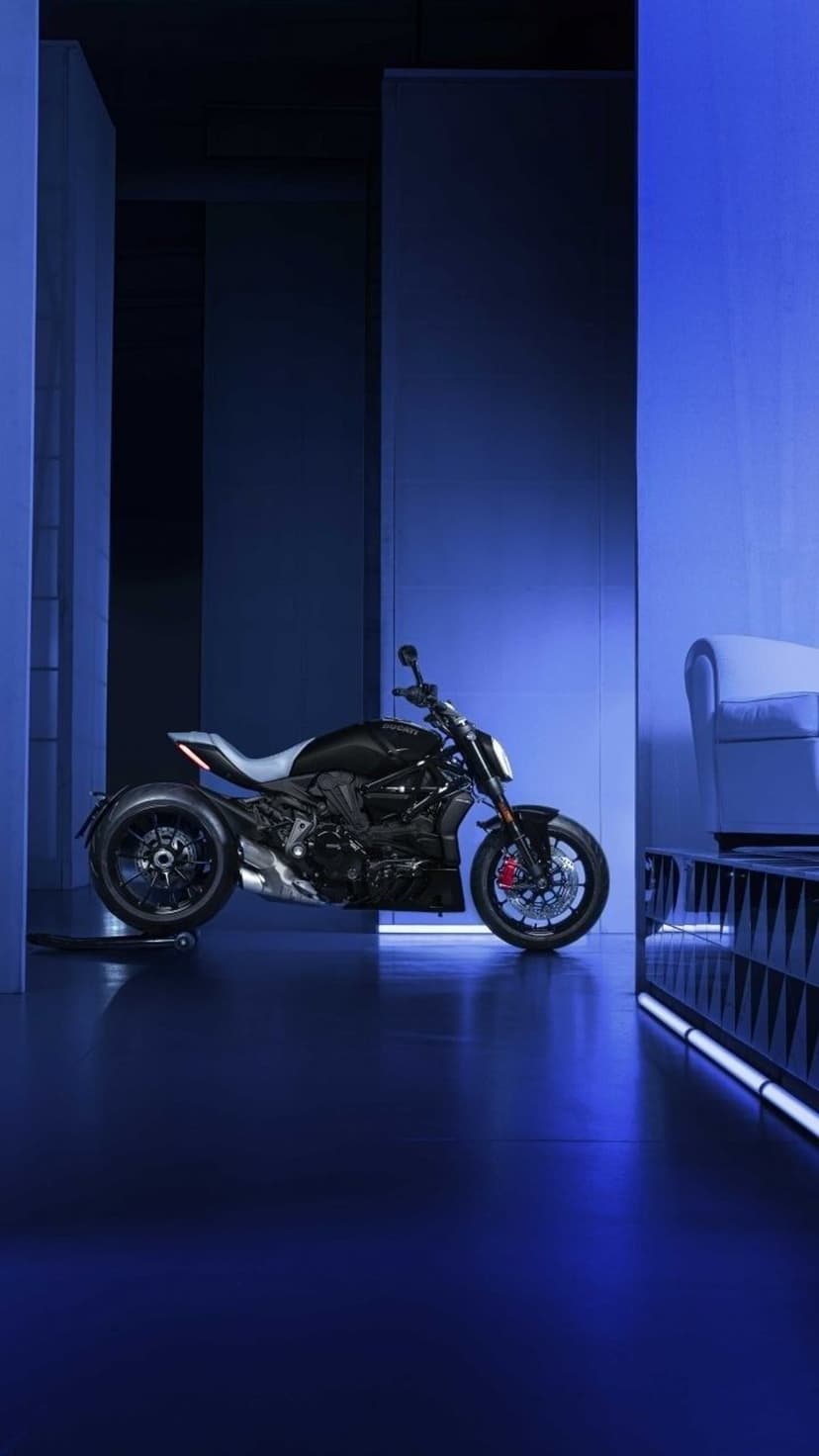 Black motorcycle with a tan seat parked in a dark studio illuminated by glowing blue neon geometric light strips.