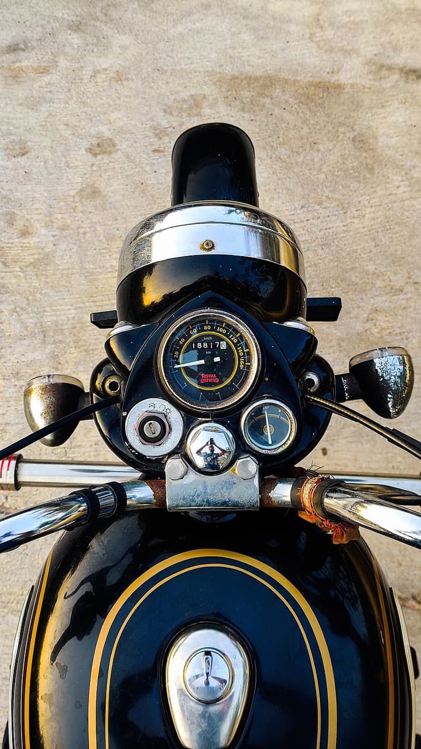 Royal Enfield motorcycle handlebars and analog speedometer with chrome finishes and gold pinstriping details.